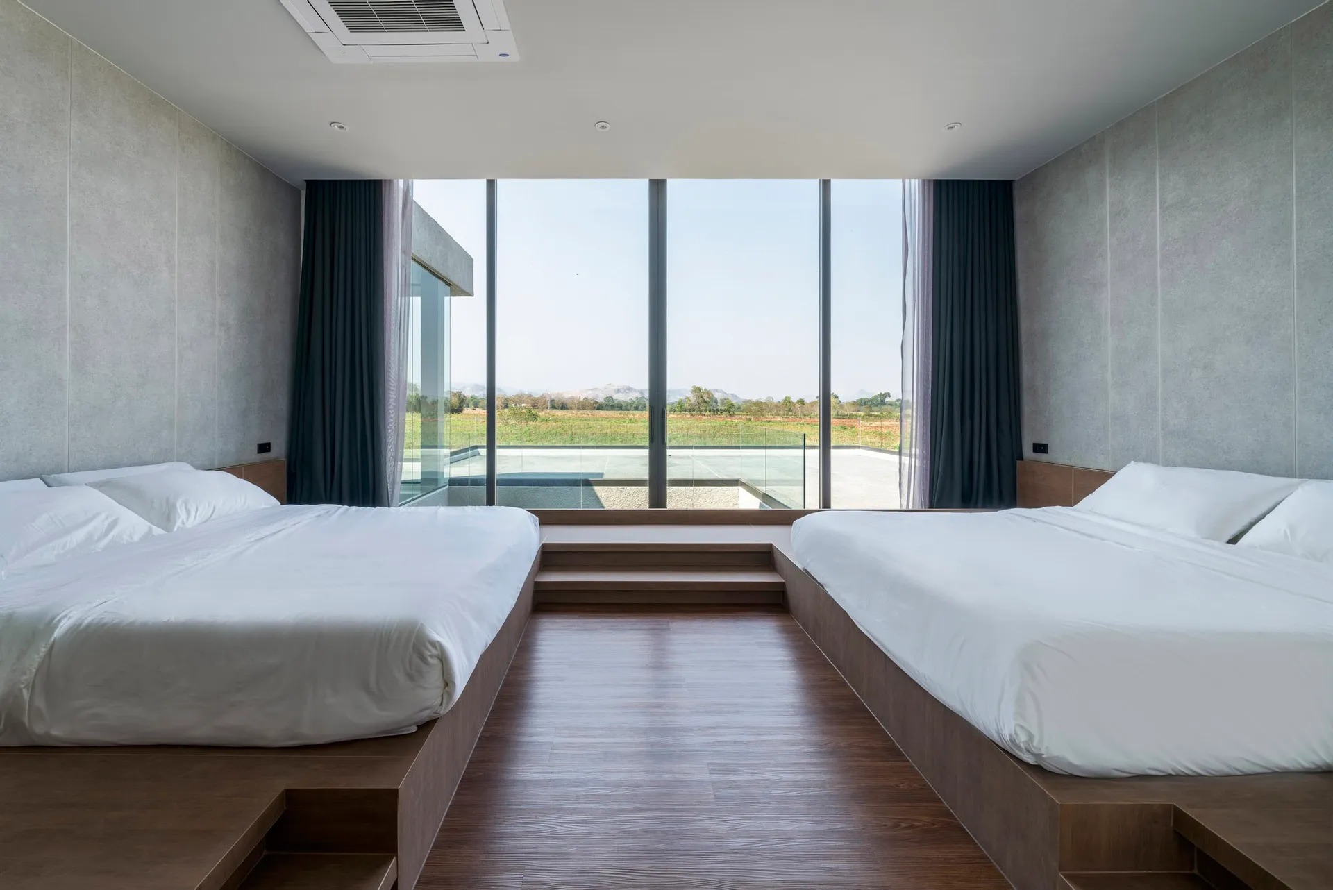 Modern, minimalist bedroom with concrete walls and polished wooden floor, featuring twin beds with wool bedding and views of
