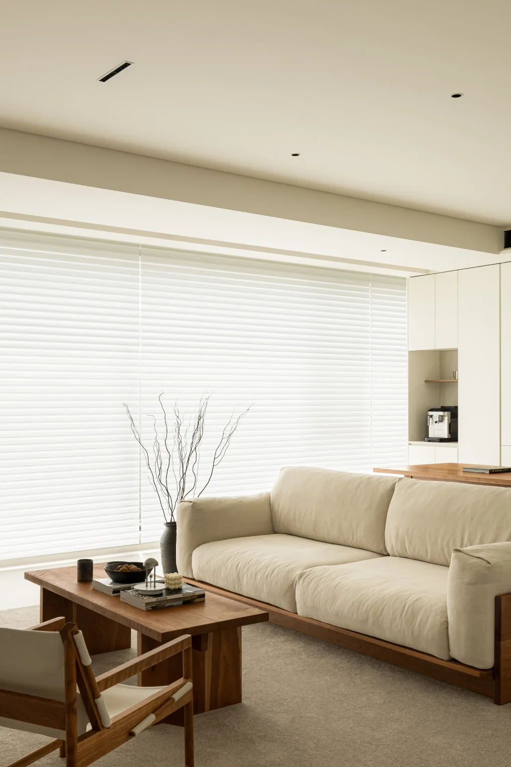 A modern minimalist living room with neutral tones, featuring a sleek sofa, wooden coffee table, and decorative vase.