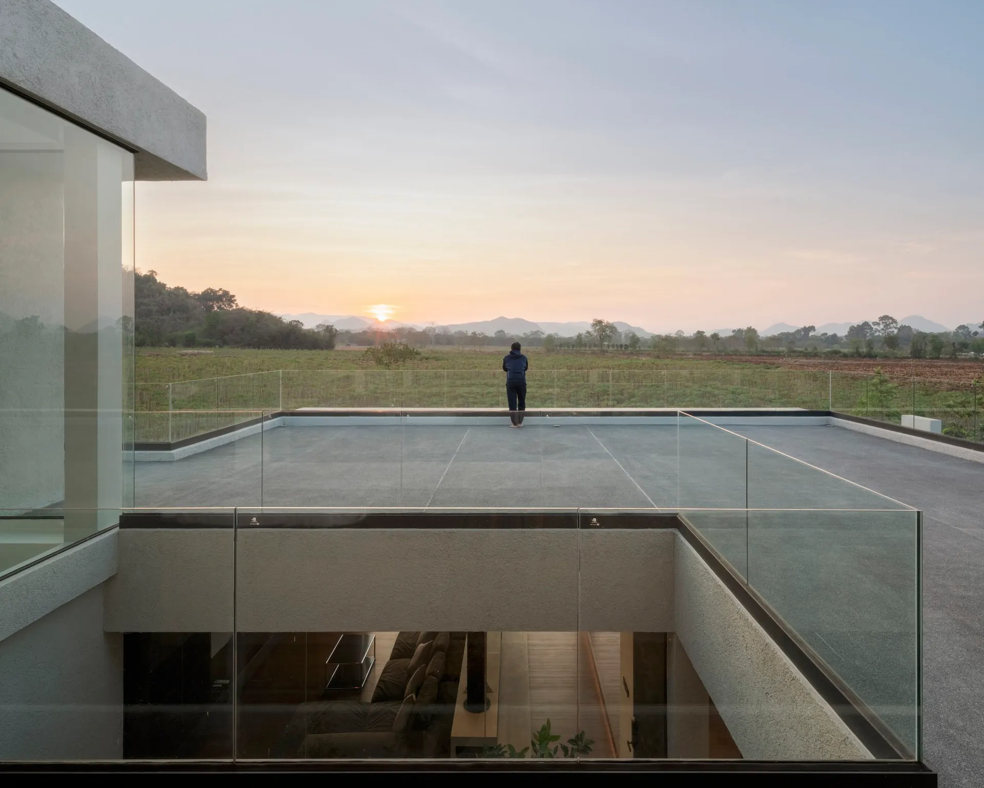 A modern residential building featuring glass walls overlooking a scenic landscape at sunset.