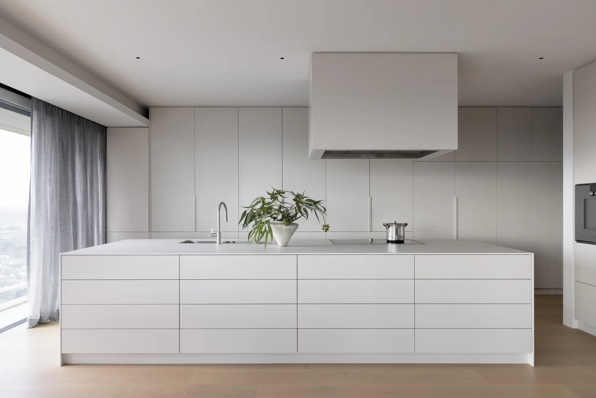 Modern minimalist kitchen with white cabinets, stainless steel appliances, and a large island.