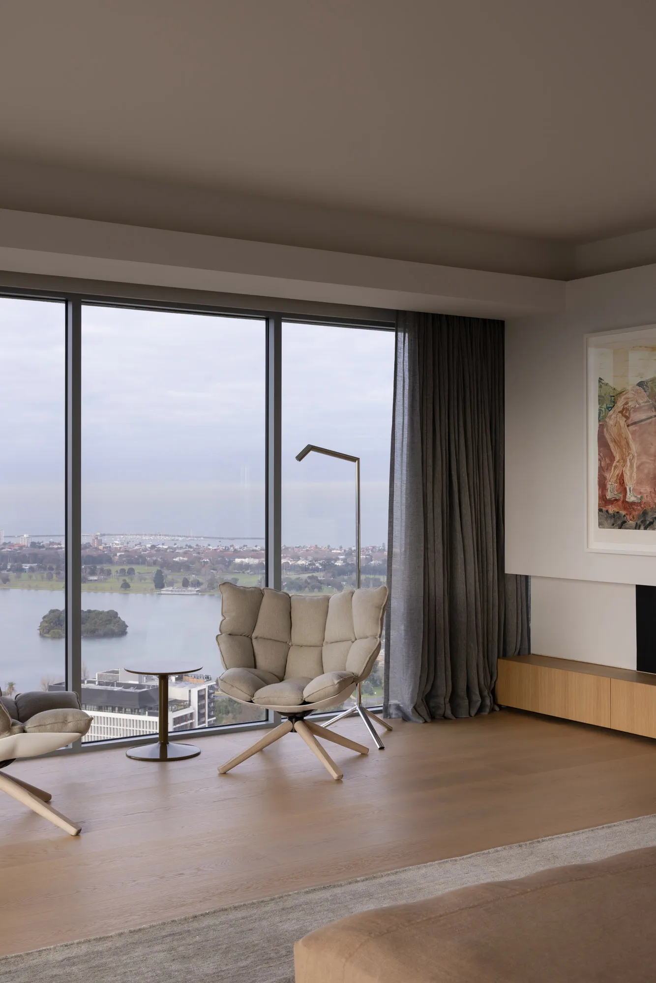 Contemporary living room featuring large windows overlooking a cityscape with wooden flooring, plush seating, and minimalist