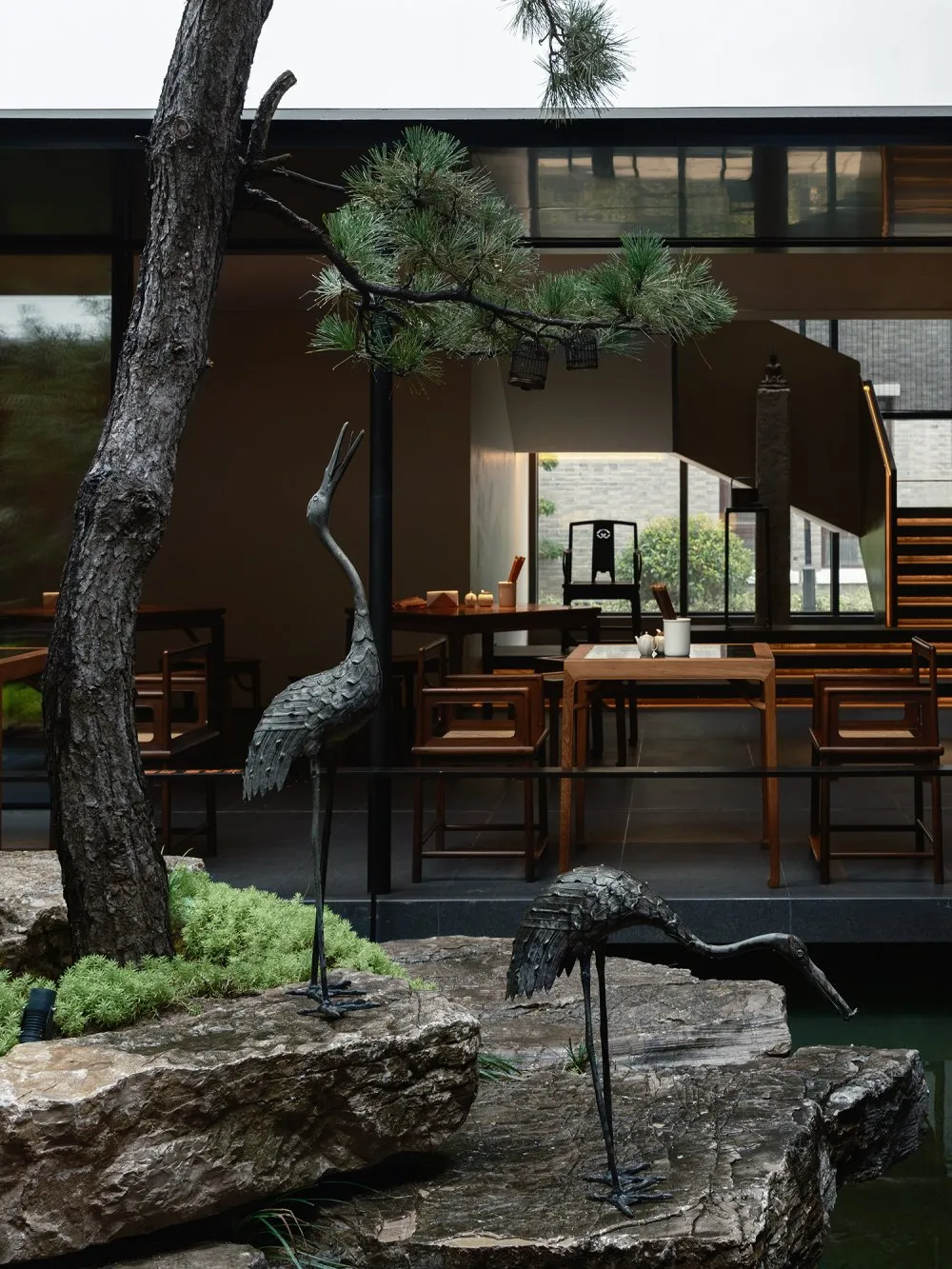 Modern restaurant interior with wooden tables, stone accents, metal sculptures, and glass features