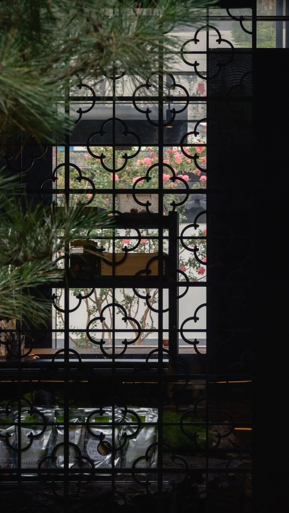 A graceful window with a black metal fence indoors, showcasing intricate geometric designs and lush greenery outside.