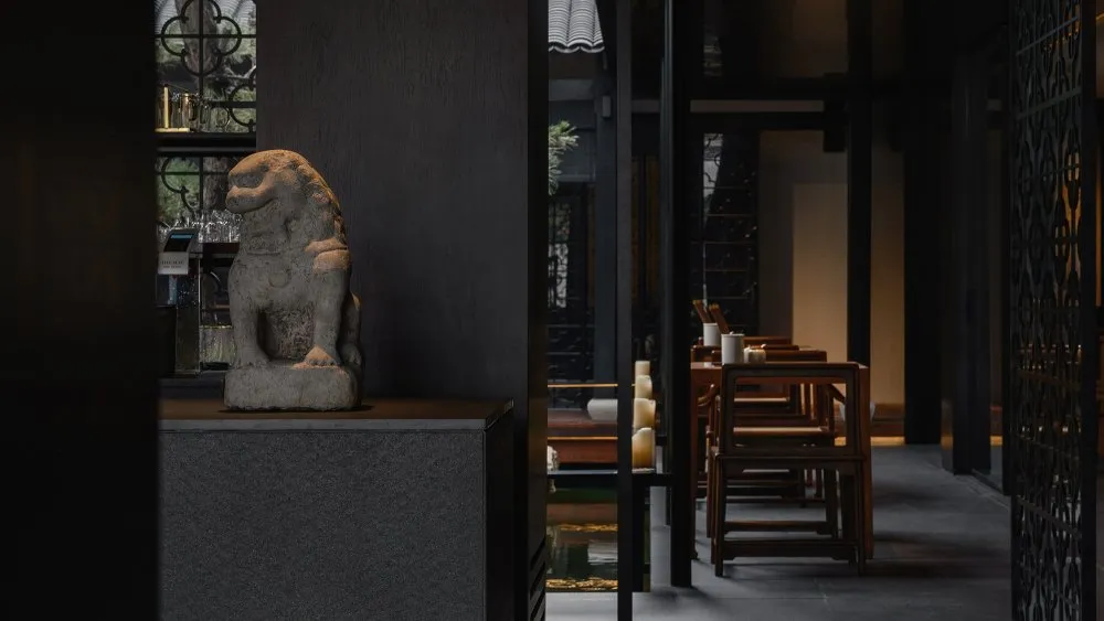 A modern restaurant interior featuring a stone lion statue and dark furnishings.