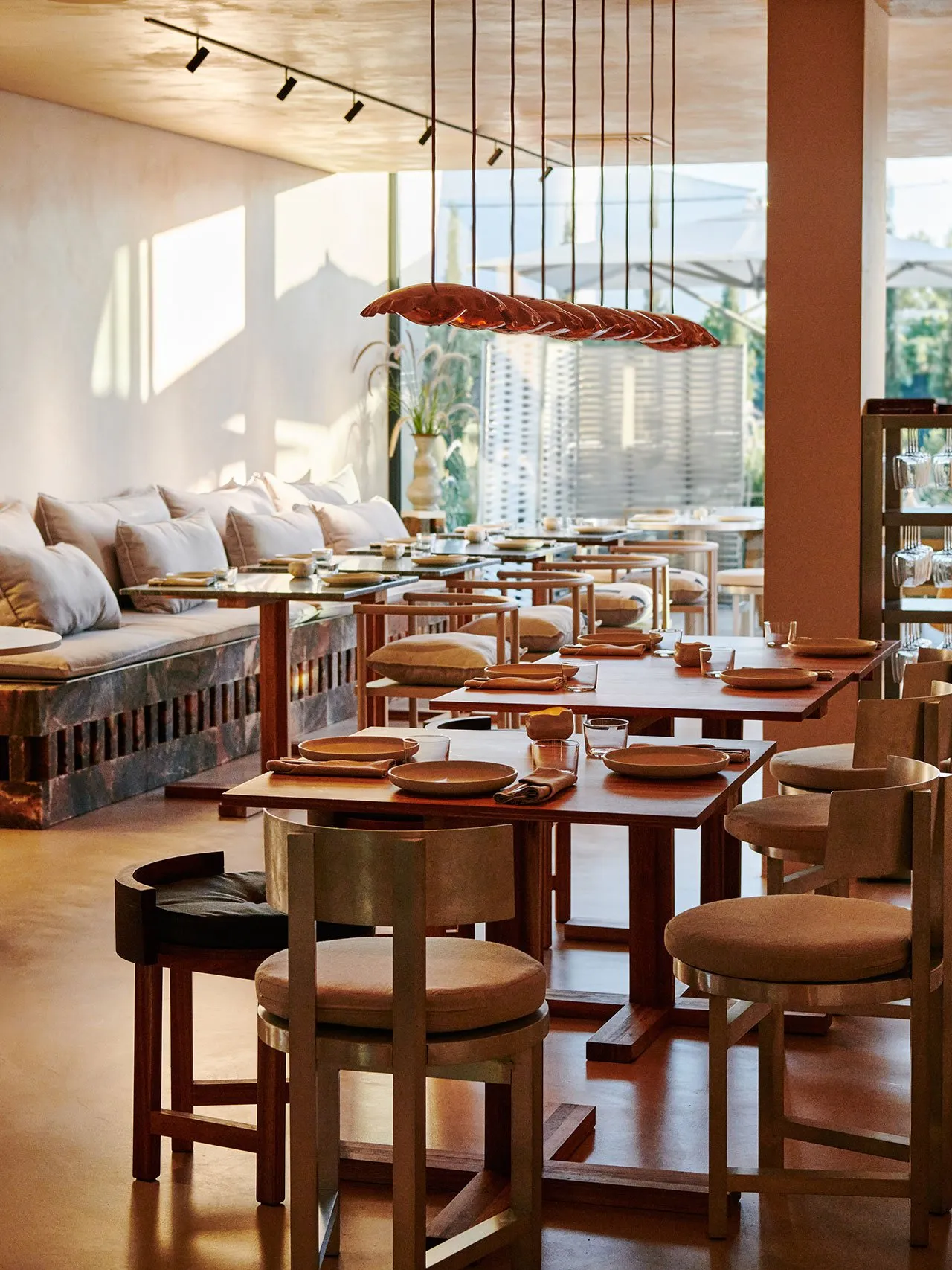 Modern restaurant interior with wooden tables, cushioned chairs, and warm lighting.