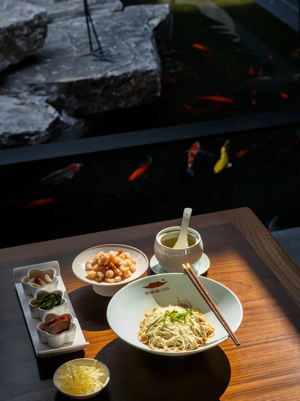 A modern restaurant setting featuring a table with a bowl of noodles, a bowl of shrimp, small dishes of various condiments, a