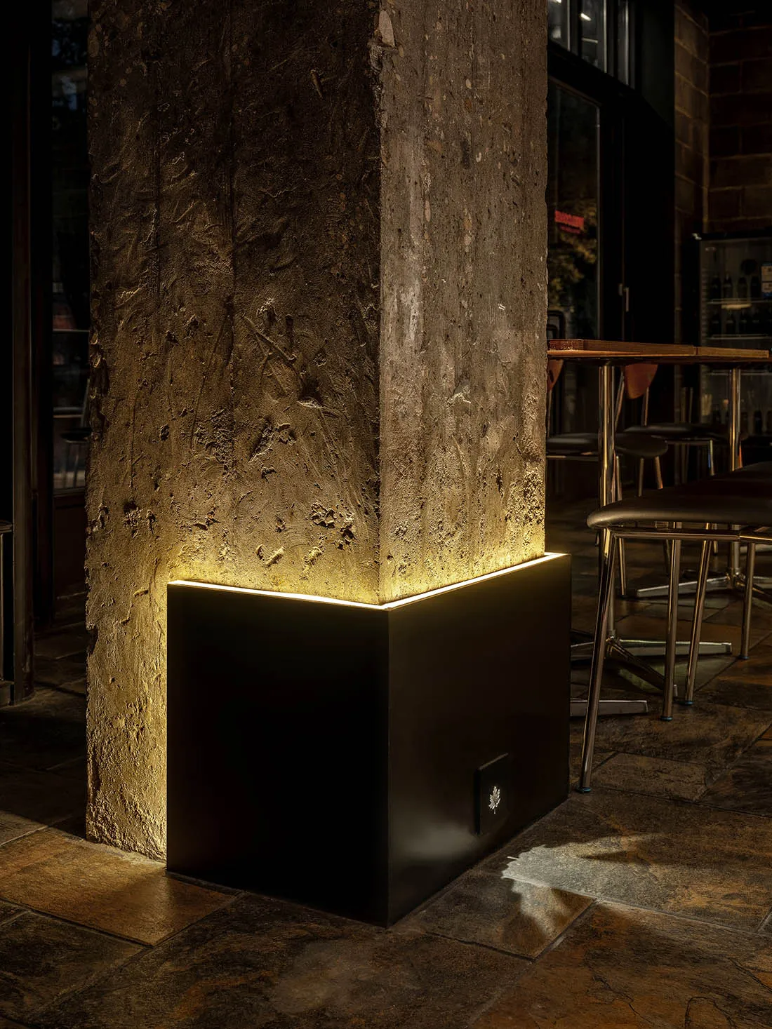 A close-up image of an industrial-style restaurant interior featuring a illuminated concrete pillar.