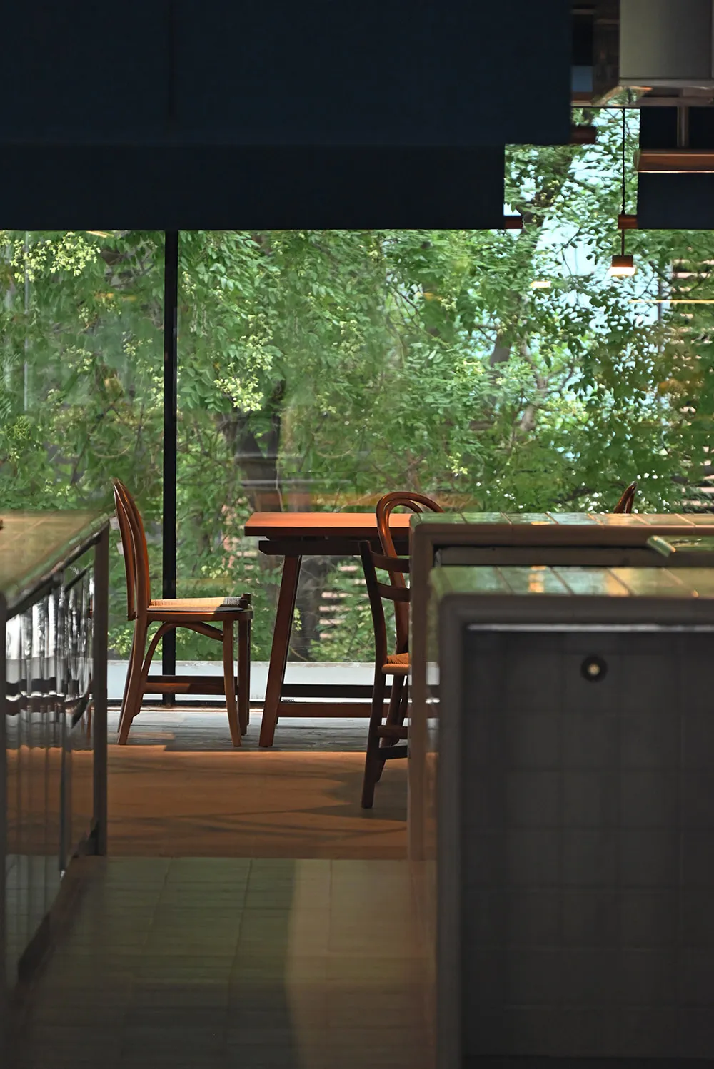 A modern coffee shop interior with wooden furniture and a view of greenery through large windows.