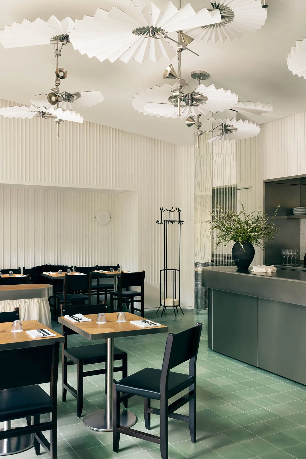Modern restaurant interior with minimalist lighting, white ceiling fans, and green tiled floor.