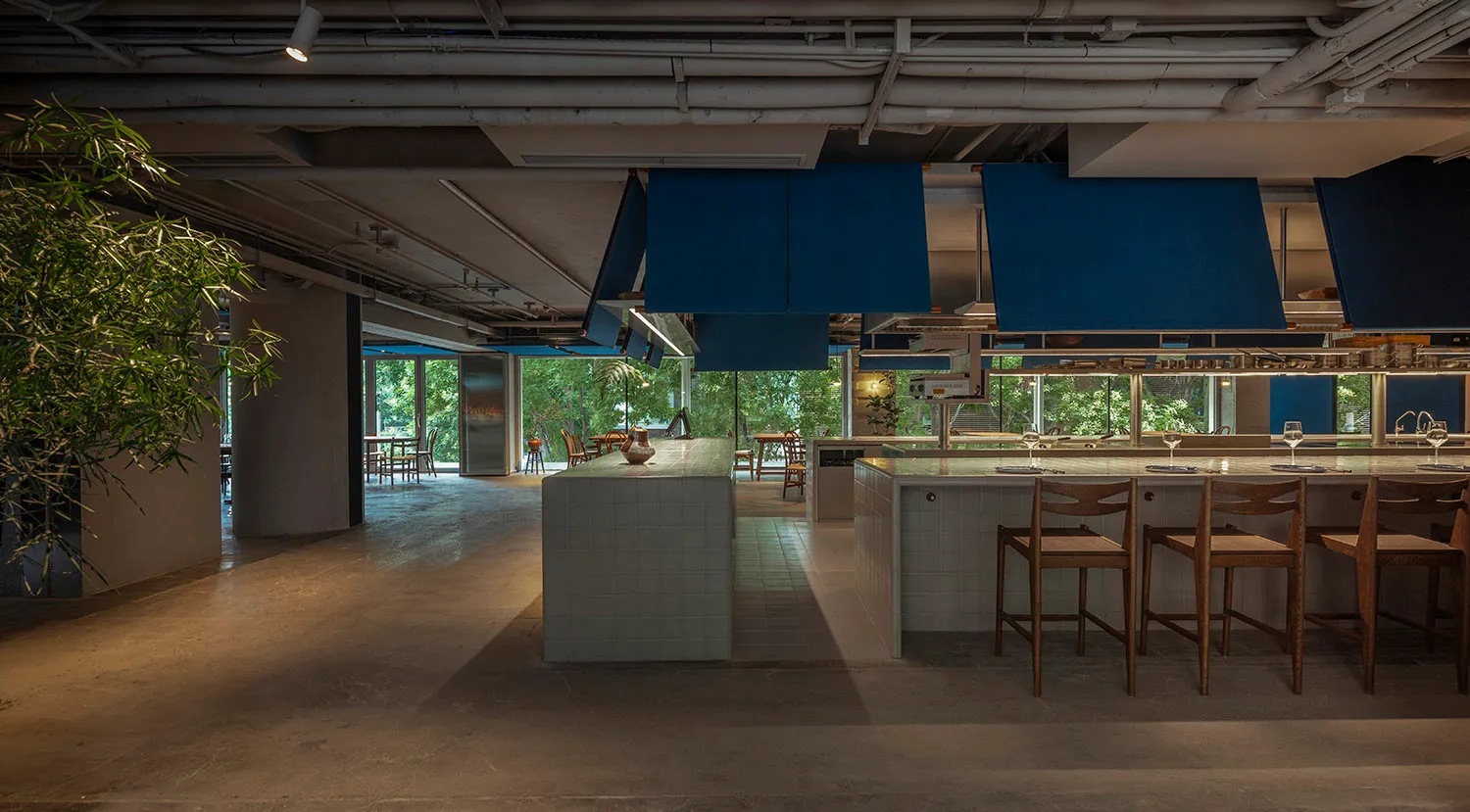 A modern restaurant kitchen with tile flooring and blue pendant lights hanging above a kitchen island.