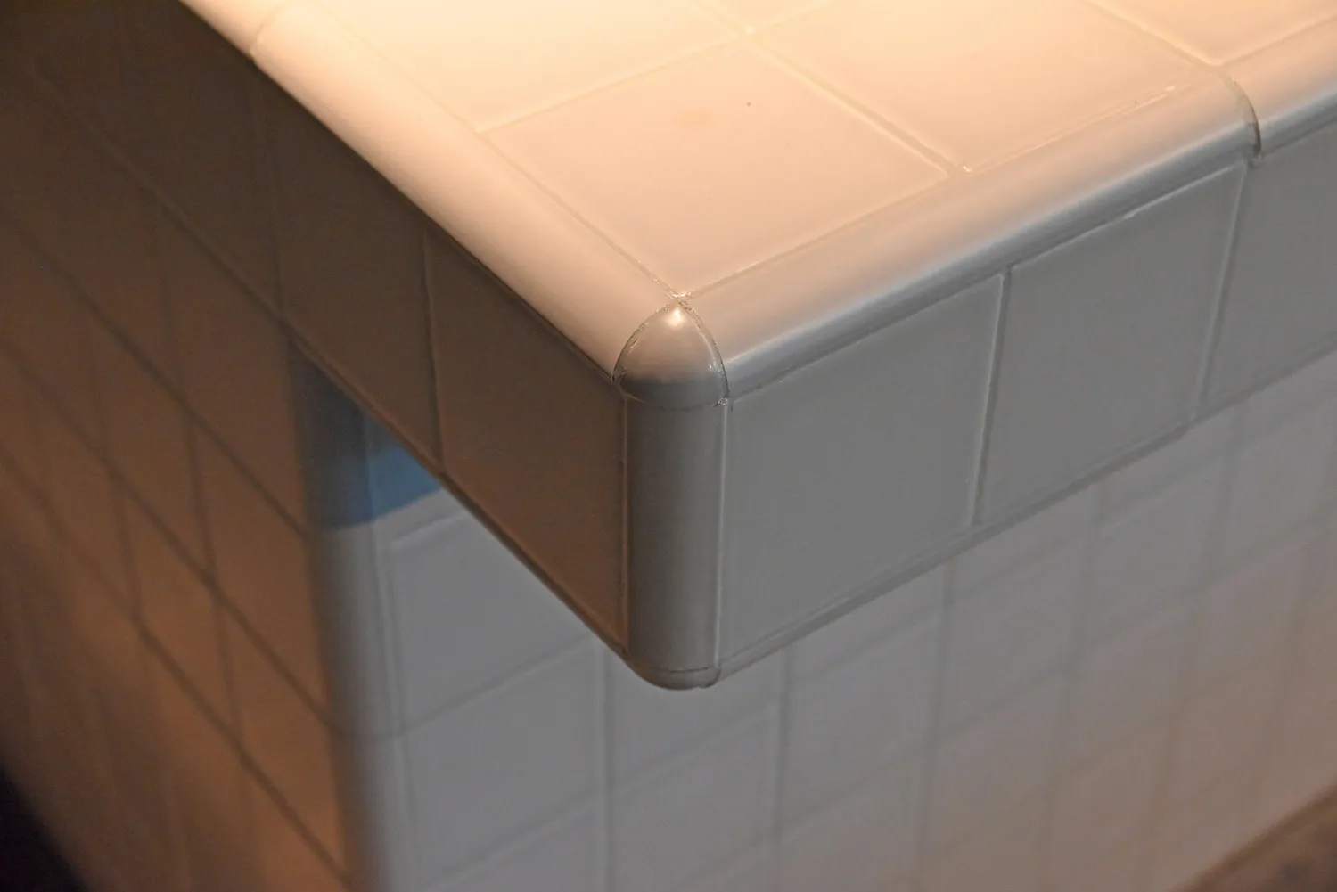 A close-up of a white tile interior wall corner with a corner protector.