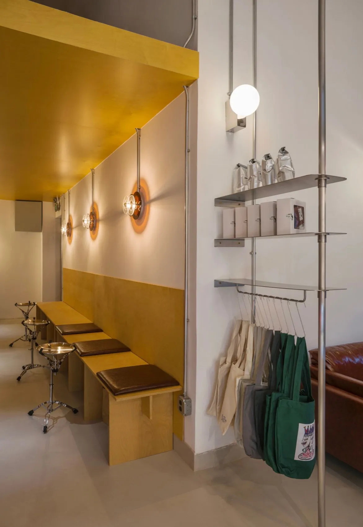 Modern cafe interior with wooden benches, concrete floor, and hanging lamps.