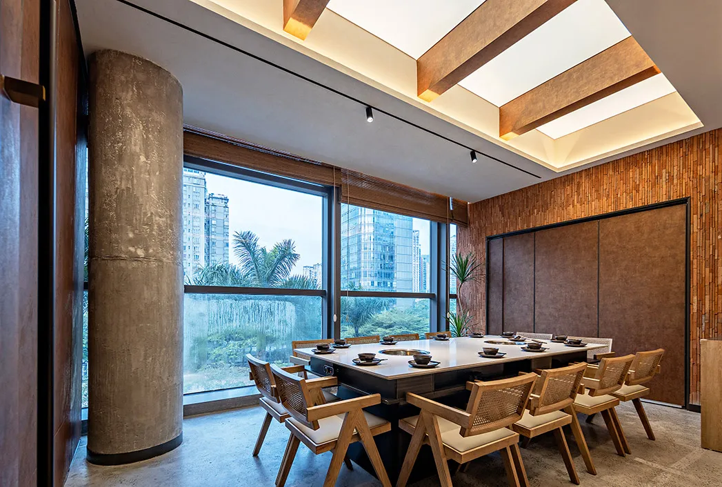 Industrial-themed restaurant interior featuring concrete walls, wooden chairs, and glass windows overlooking a cityscape.