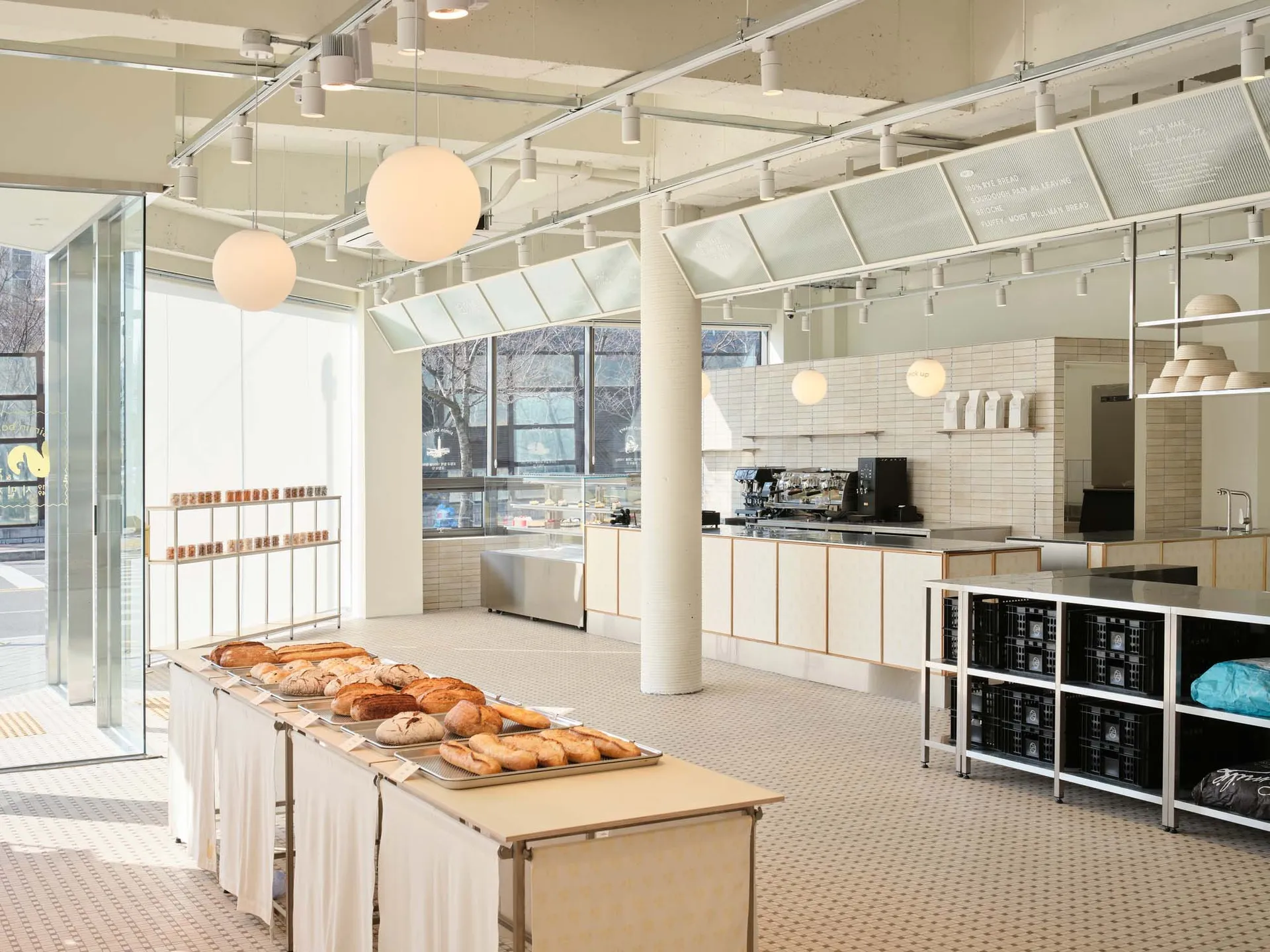 A minimalist bakery interior with concrete and glass elements showcasing a variety of bread items on display.