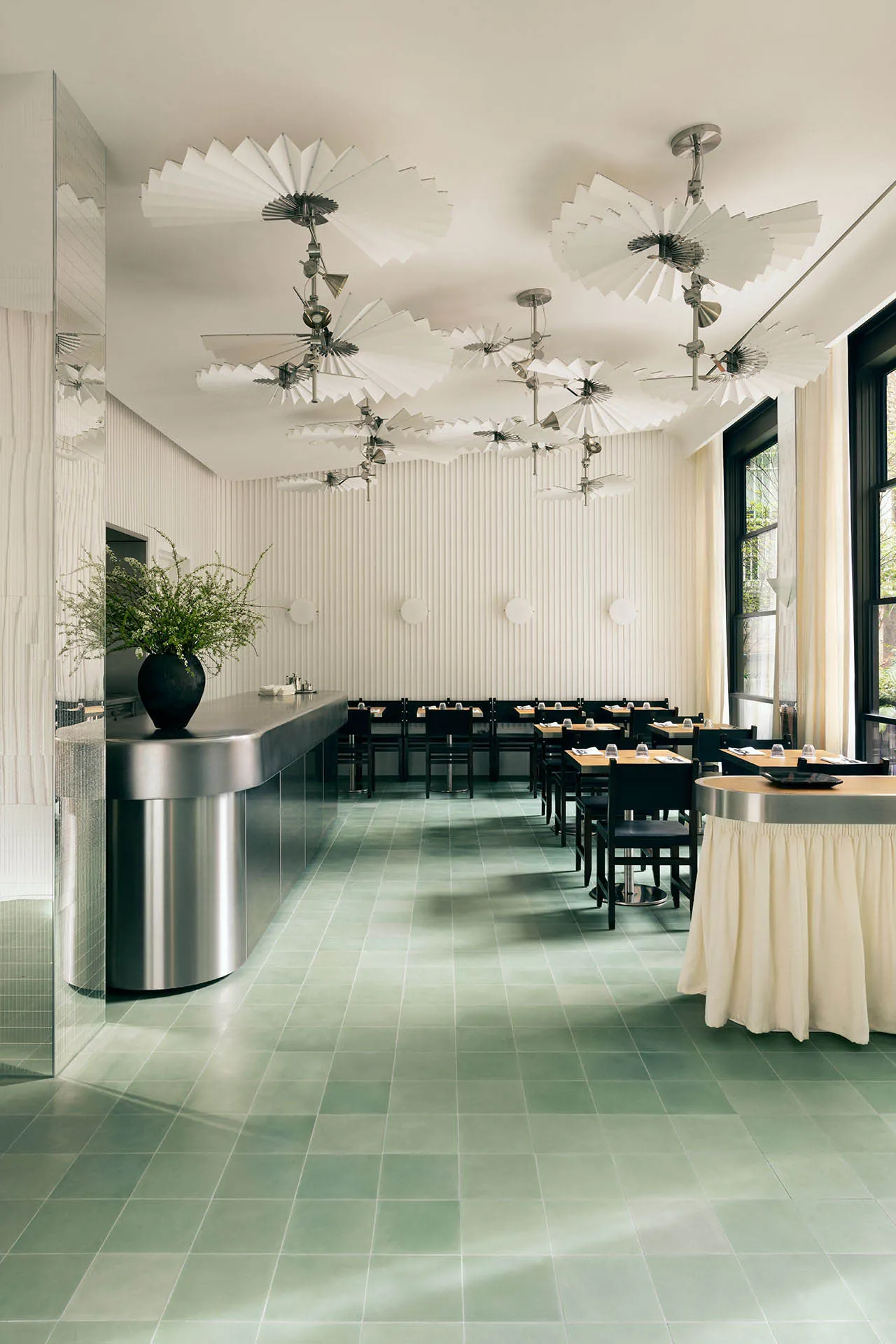 A modern cafe with green tiles and white walls, featuring a sleek black counter and stylish hanging light fixtures.