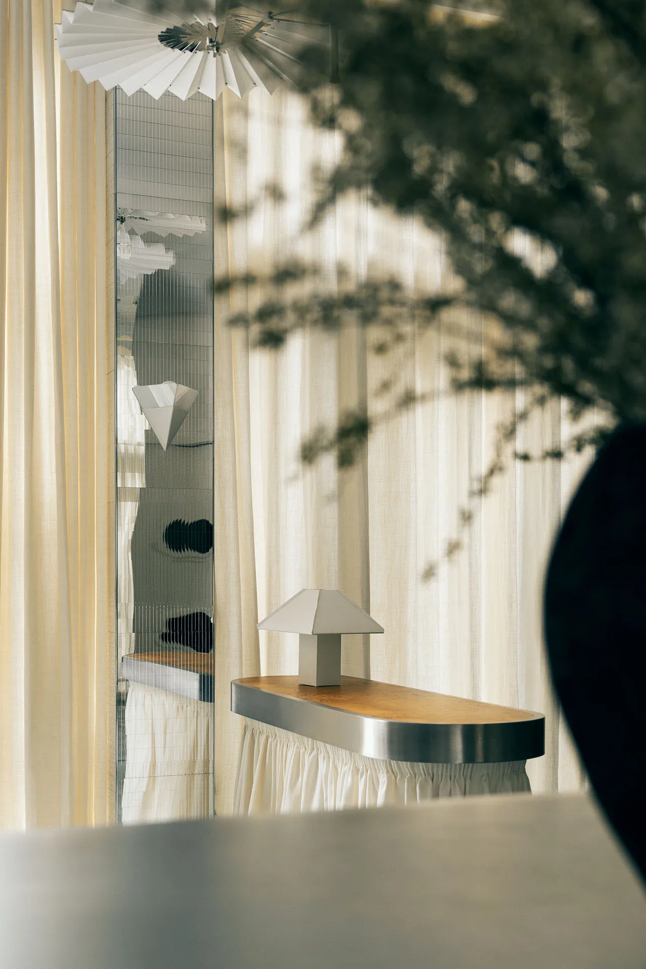 A modern entryway with a white metal and wooden console table, white curtains, and a white lamp.