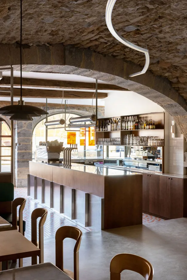 A minimalist café interior featuring wooden furniture, stone ceiling, and glass displays.