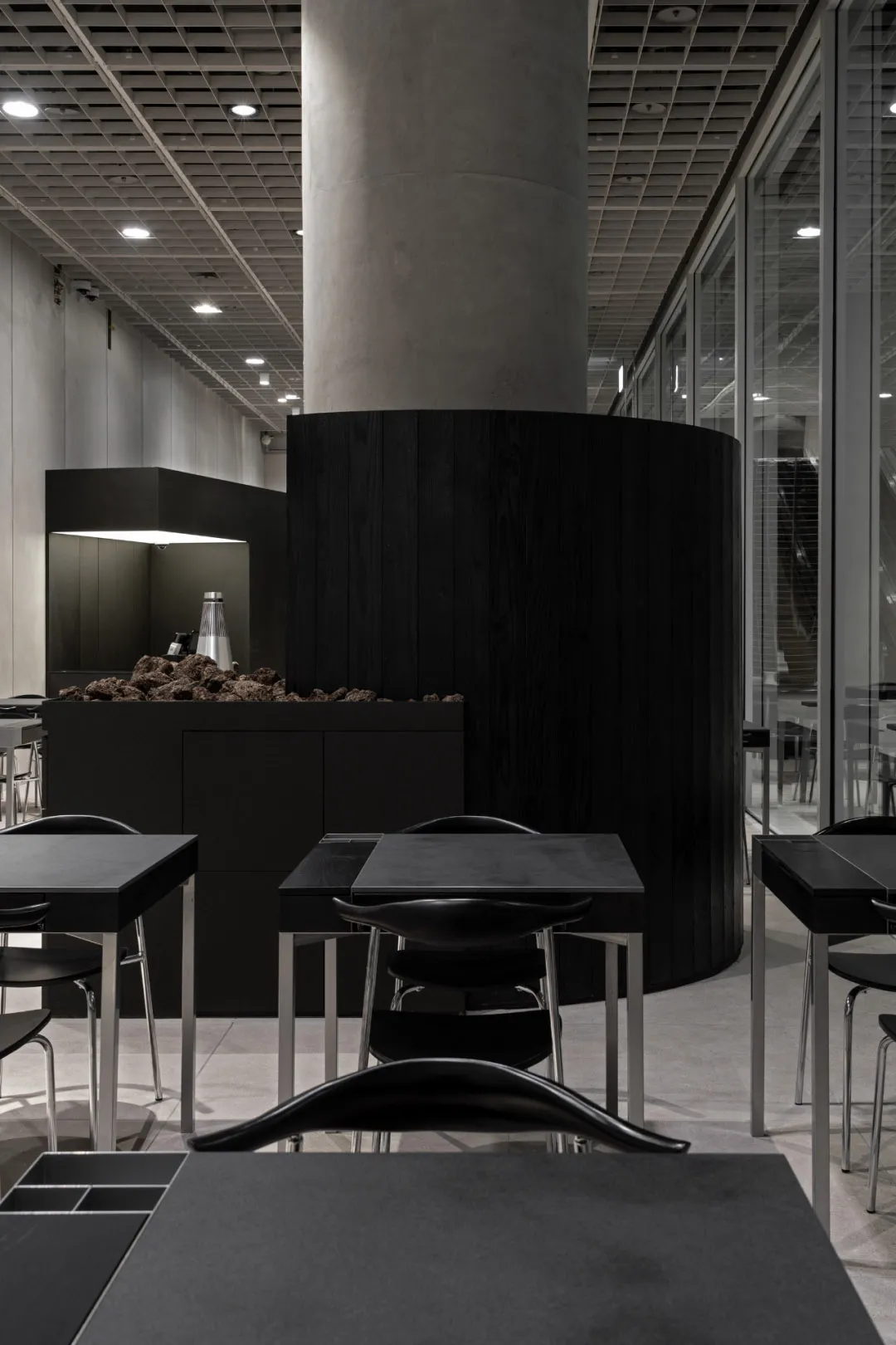 Modern minimalist interior of a coffee shop with black tables, chairs, and wood paneling.