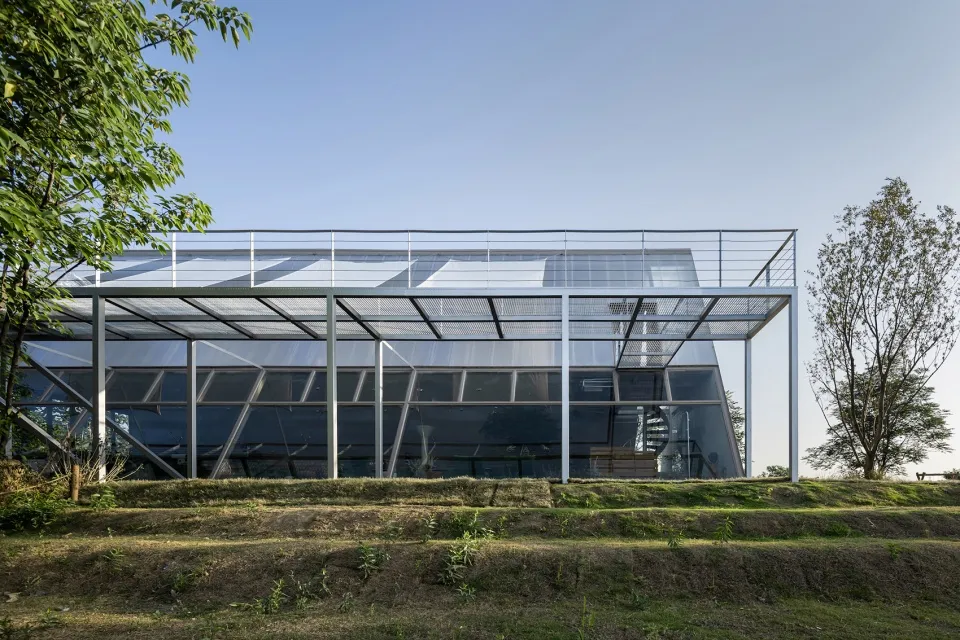 一座現代玻璃建築採用極簡設計,位於戶外,背景有綠意植栽。