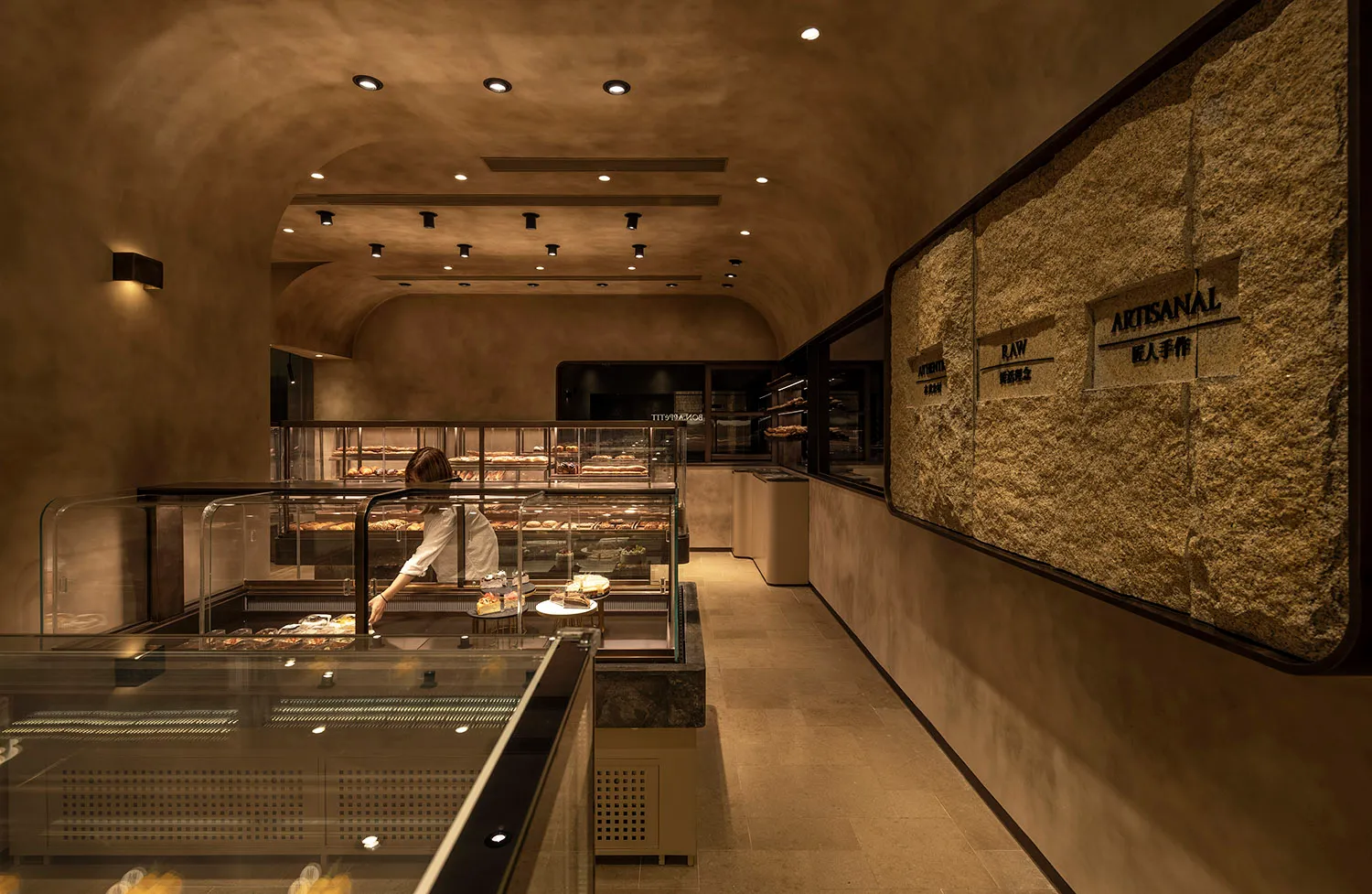 Interior of an artisan bakery with stone walls, concrete flooring, and glass display cases.