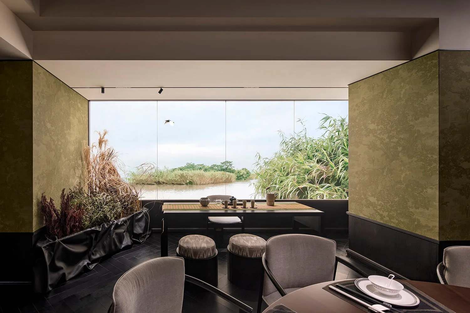 Modern restaurant interior with wooden table and chairs, overlooking a serene lake.