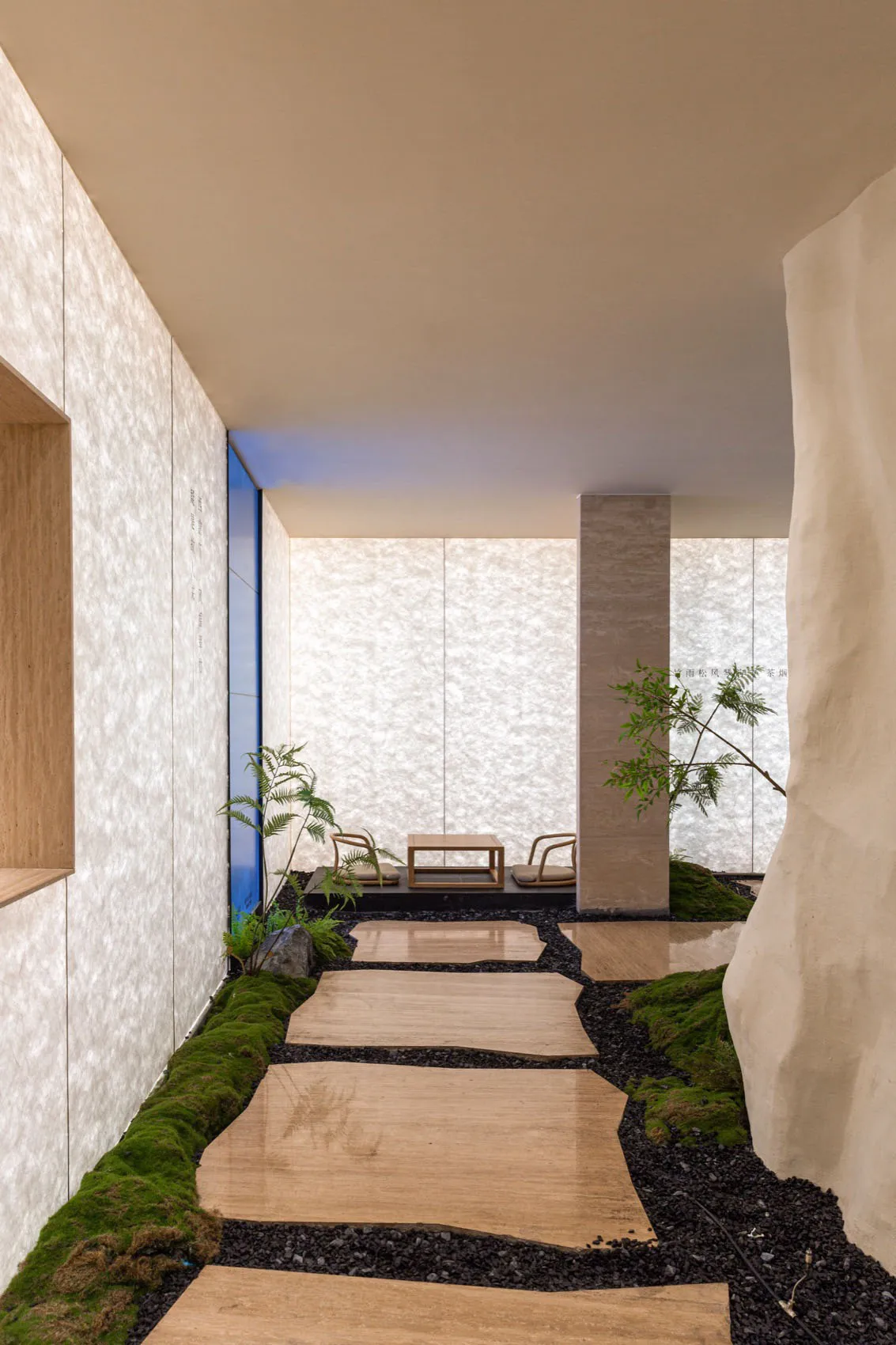 A minimalist courtyard with wooden stepping stones and a small table and chairs under a covered area.