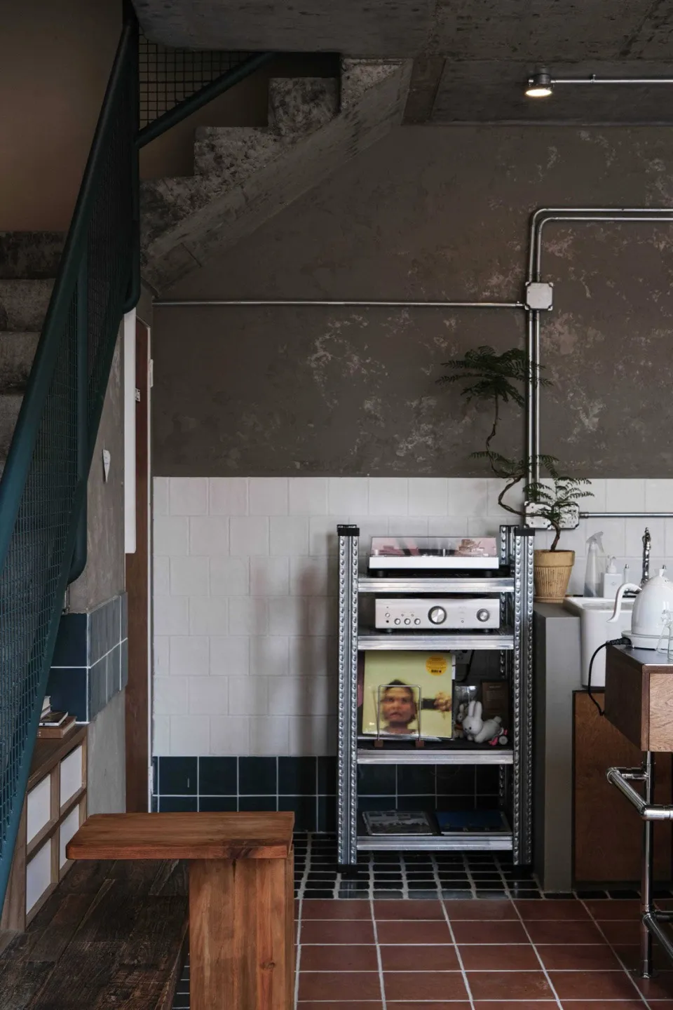A kitchen with industrial design elements, featuring concrete and metal materials, including a metal shelf unit with various