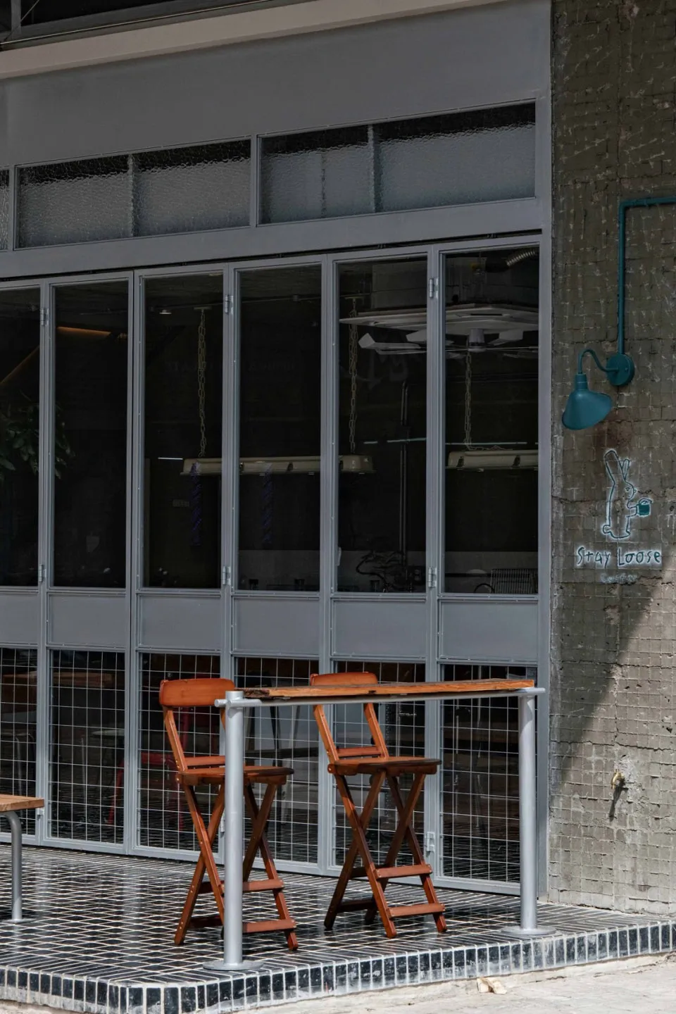 街邊咖啡廳的戶外座位區,採用工業風設計元素,包含木質家具、金屬欄杆與大型玻璃窗