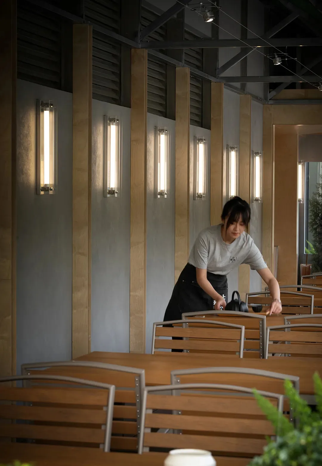 一位女性在現代餐廳室內清潔木製餐桌,搭配幾何造型燈具。