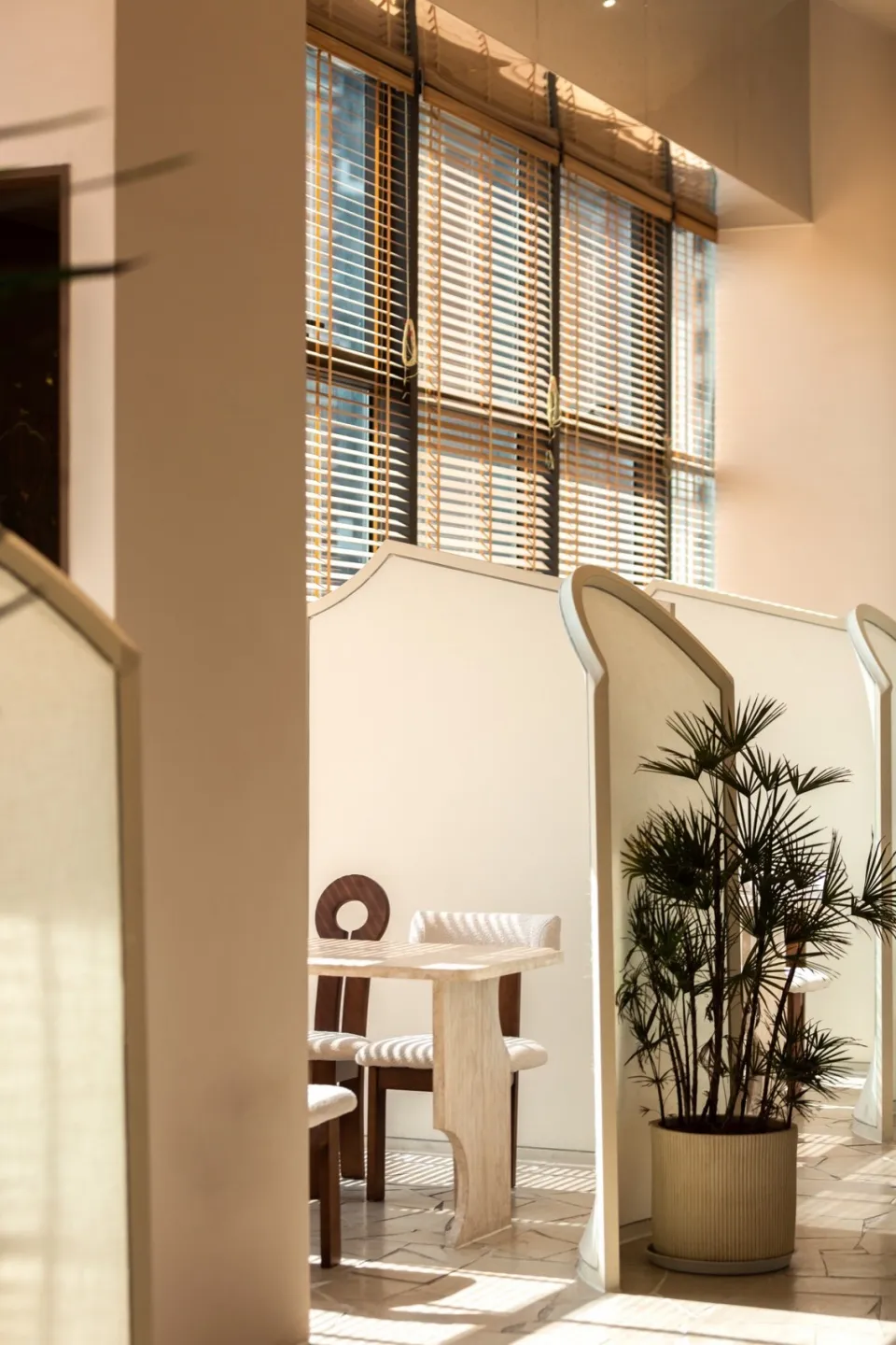 A modern restaurant interior featuring a neutral-toned color palette, natural lighting through tall windows, and a cozy seati