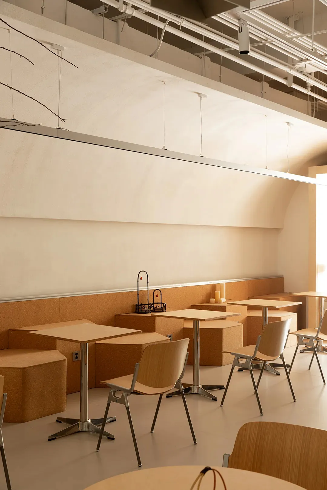 Modern cafeteria with minimalist design featuring wooden and cork tables and chairs.