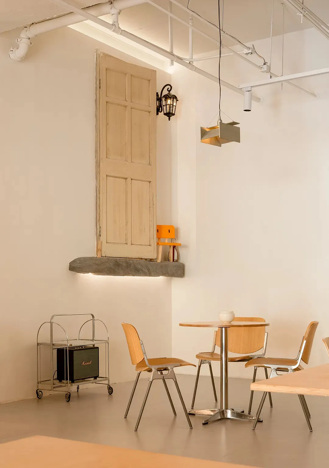 Interior of a modern restaurant featuring minimalist design elements like wooden tables, metal chairs, and concrete floor.