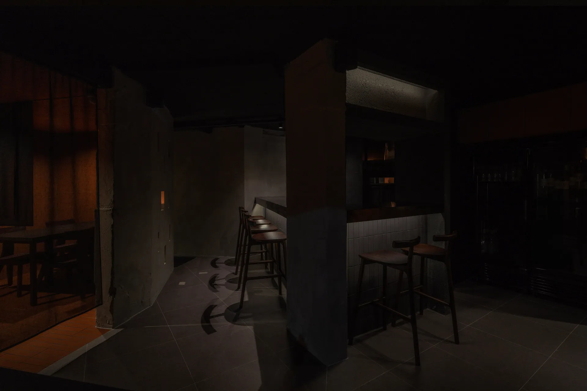 A minimalist bar interior featuring wooden stools, concrete walls, and metallic accents.