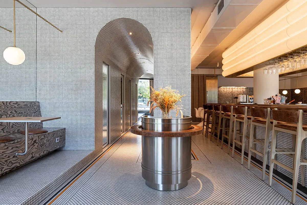 Modern cafe bar interior with metallic structures, ceramic tile floors, and wooden seating.