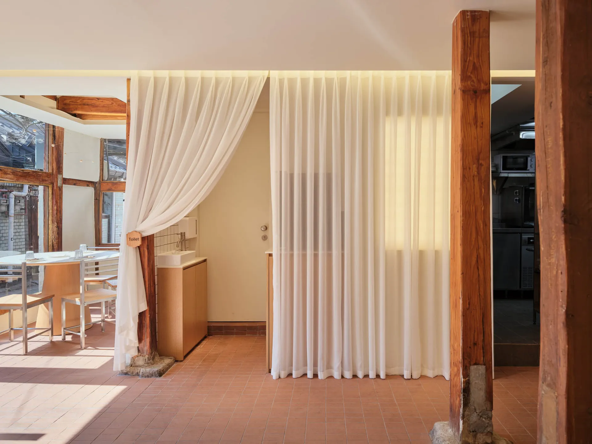 A modern restaurant interior featuring a toilet area with curtain lighting and wooden beams