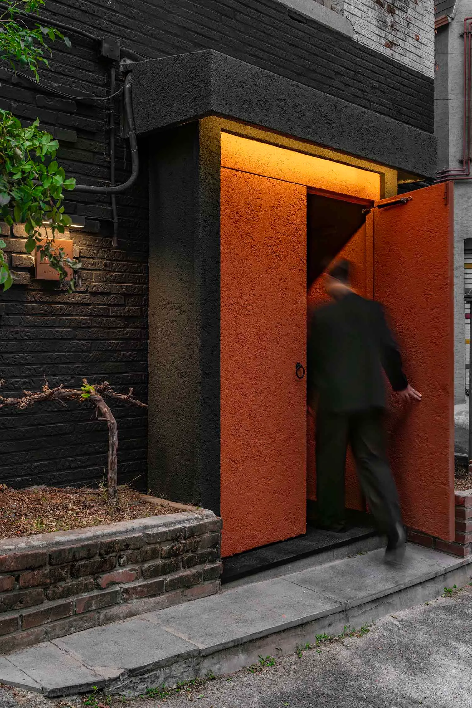 A person entering a building through a large, wide, red-brick entrance with illuminated light within.