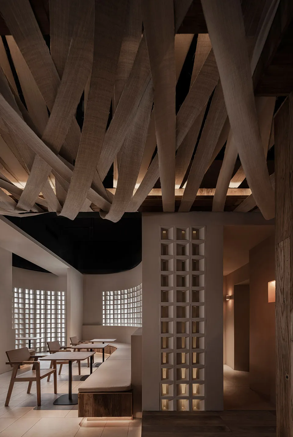 A minimalist restaurant interior featuring wooden tables, chairs, and ceiling beams.