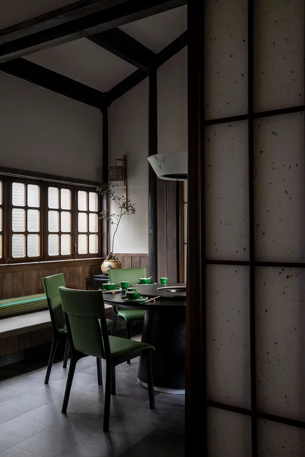A modern restaurant interior featuring a round wooden table surrounded by green upholstered chairs, set against a backdrop of