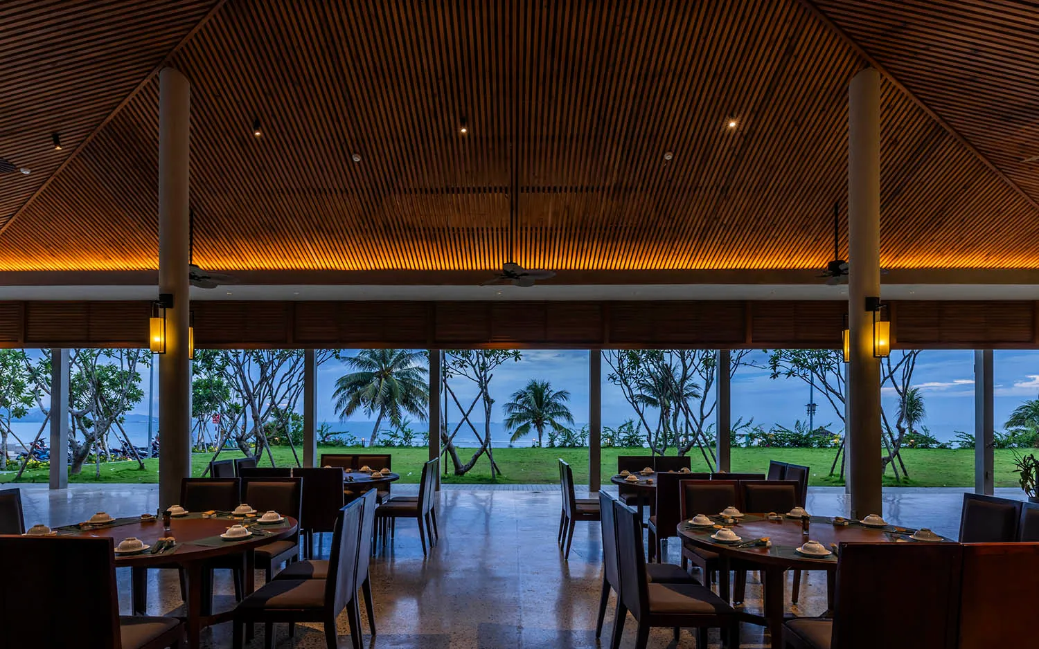 A modern restaurant interior with wooden ceiling and glass walls overlooking the coast.