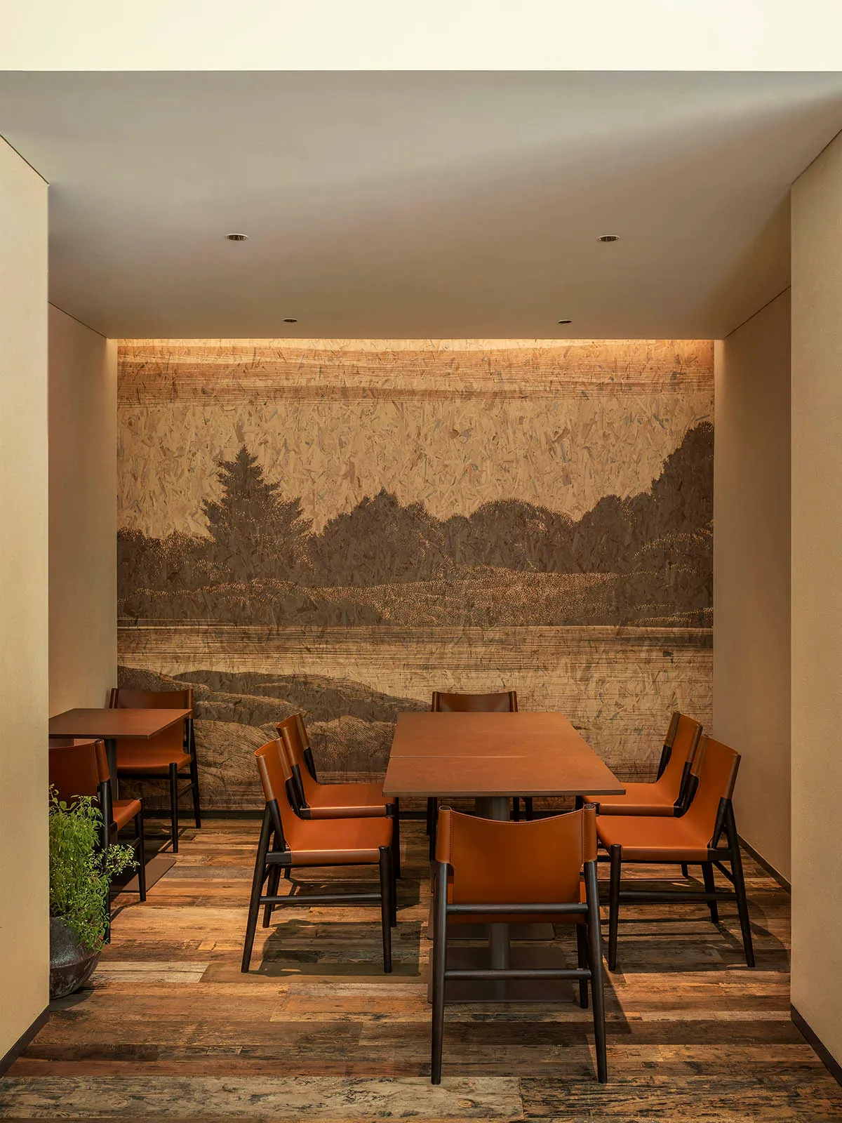 A modern restaurant interior featuring wooden tables and chairs with leather upholstery, a scenic mural on the wall depicting