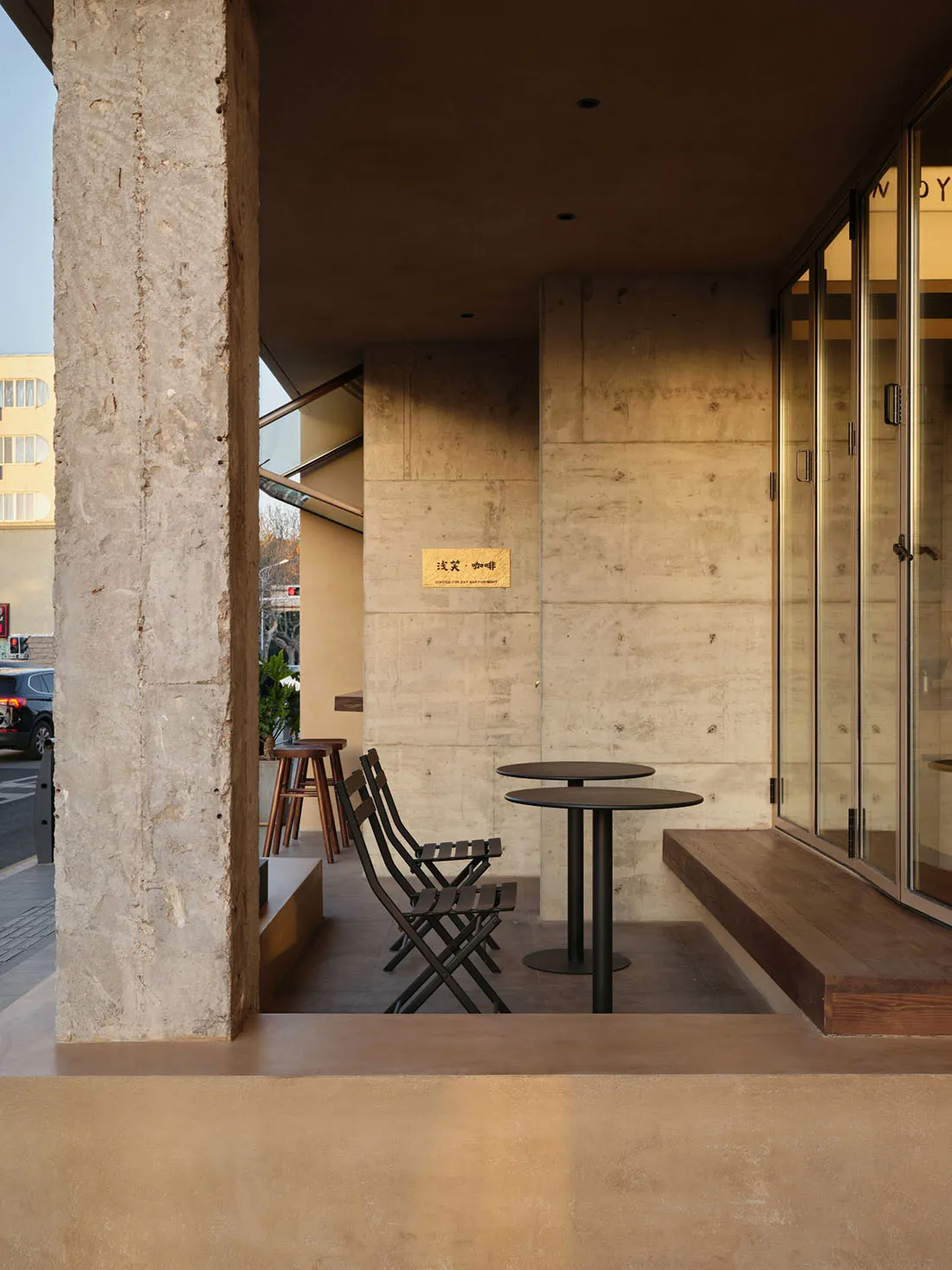 A modern cafe exterior with a concrete facade, featuring tables and chairs.