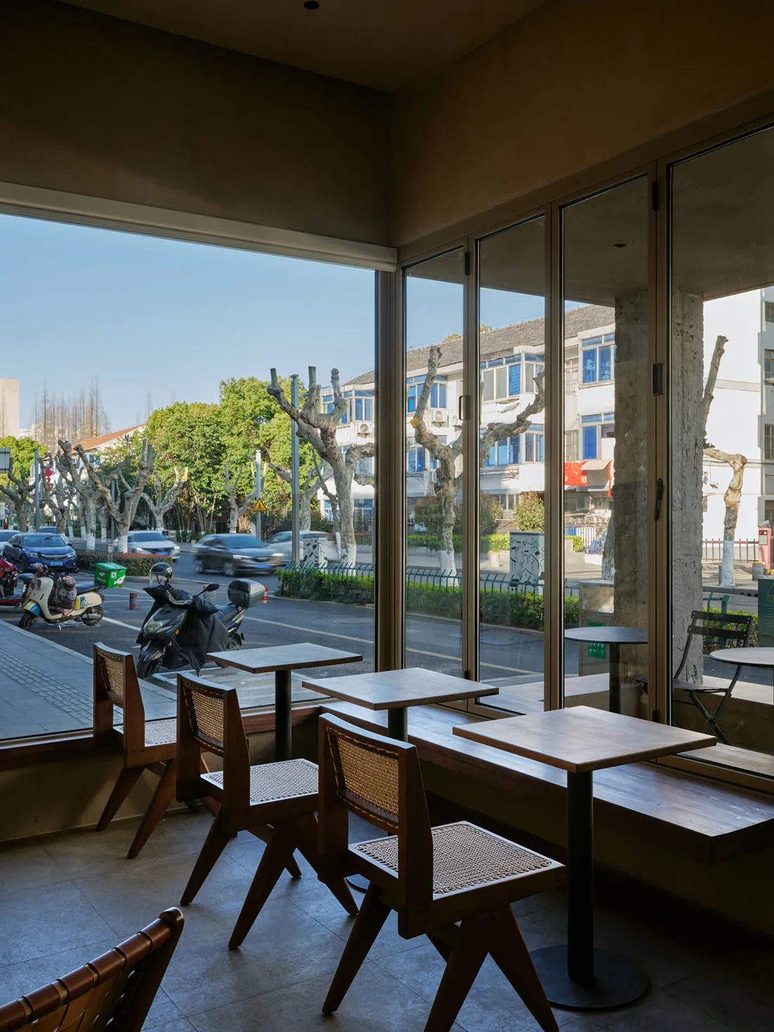咖啡廳室內擺放木質餐桌,搭配玻璃牆面,可眺望街景。