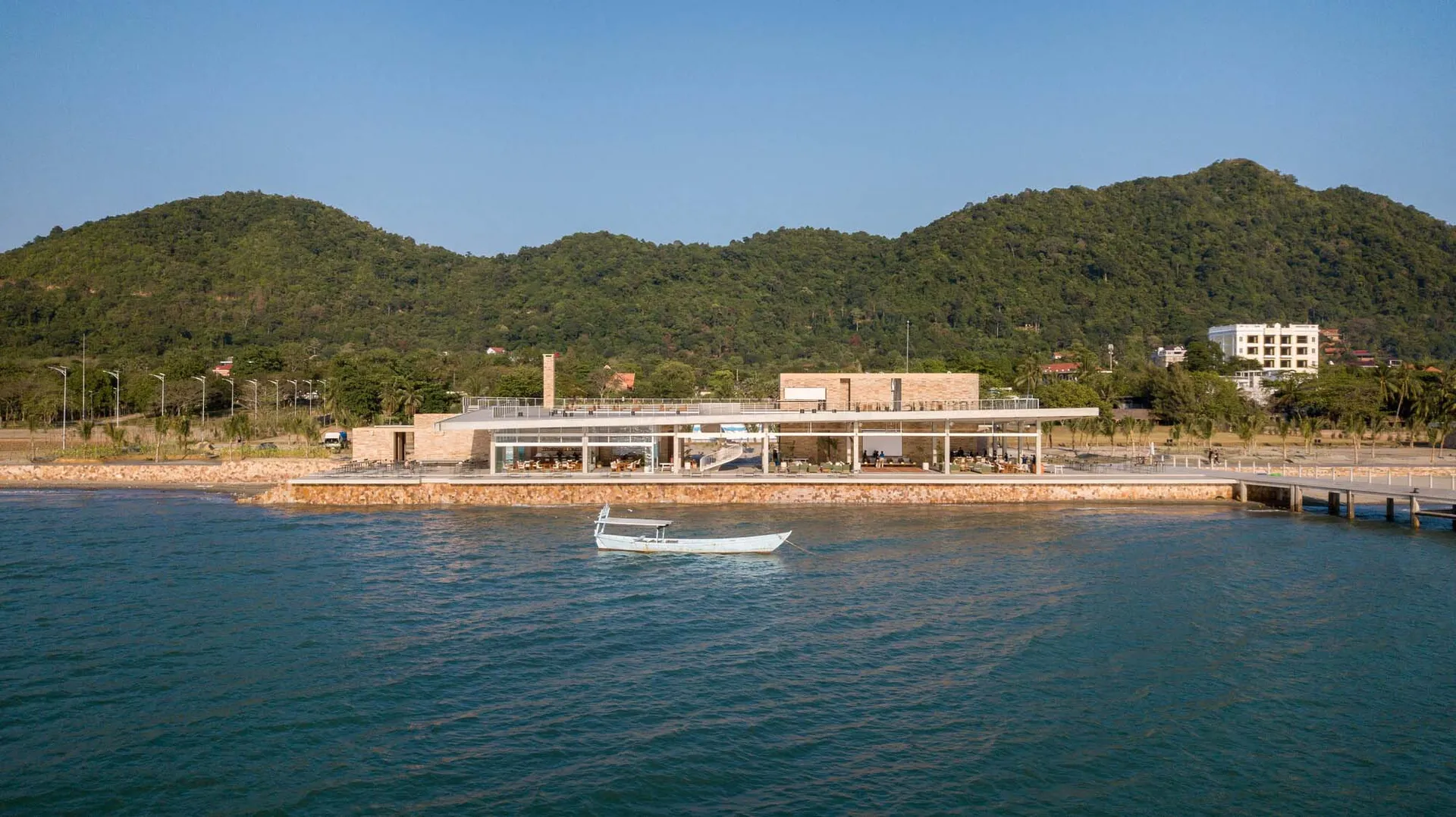 現代度假村入口,採用磚與混凝土結構,搭配大型懸挑屋簷,前景可見一艘小船。