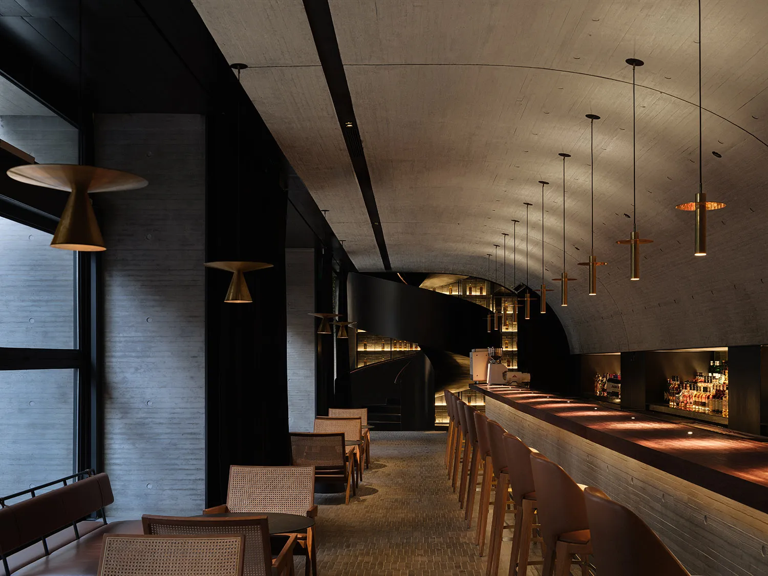 Modern minimalist restaurant bar with concrete walls, wooden seating, and pendant lights.