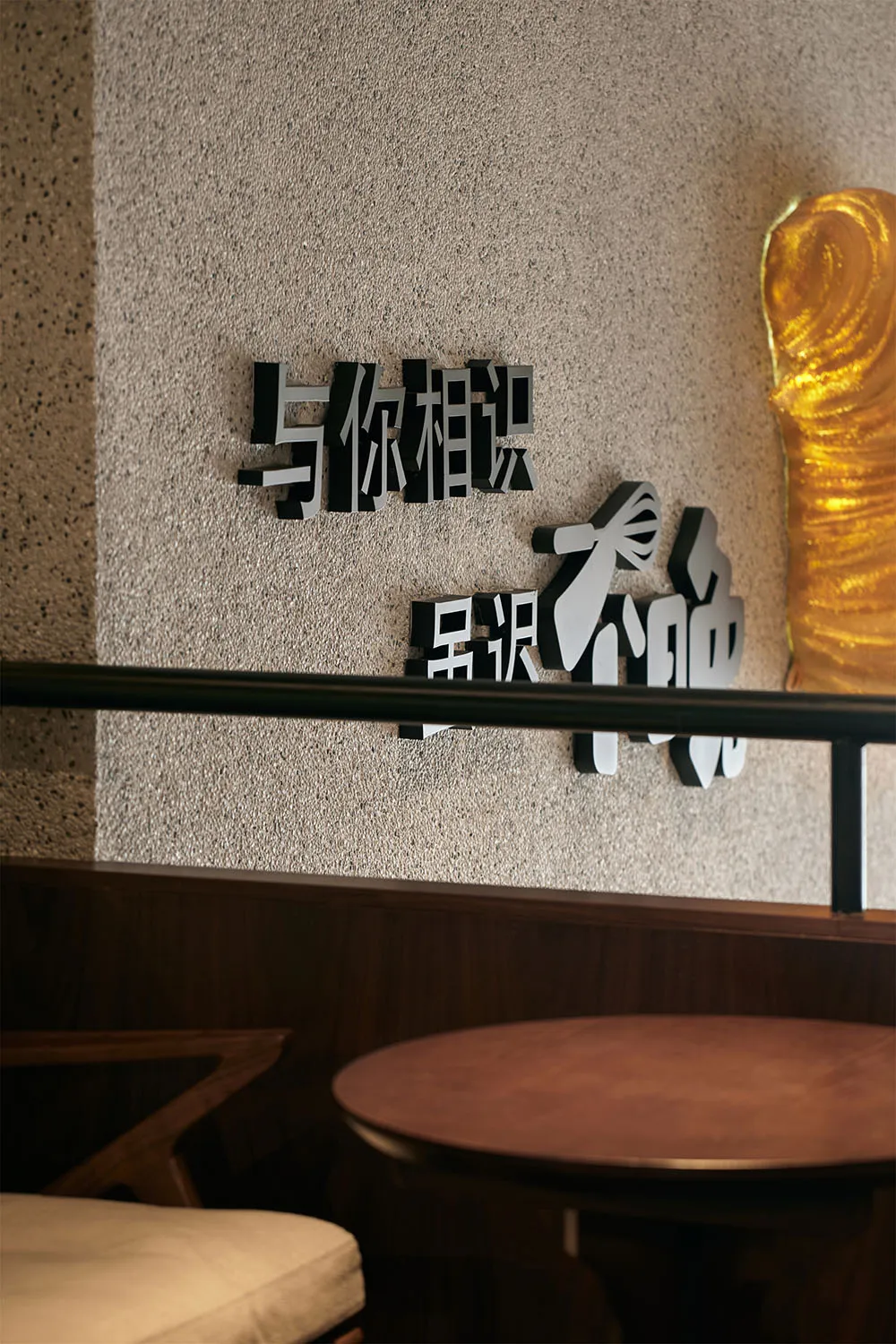 The image shows a wall art piece consisting of metallic Chinese characters displayed on a textured beige wall.