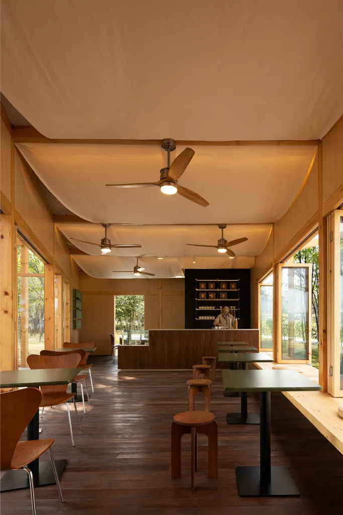A modern cafe bar interior with wooden furniture and fans on the ceiling.