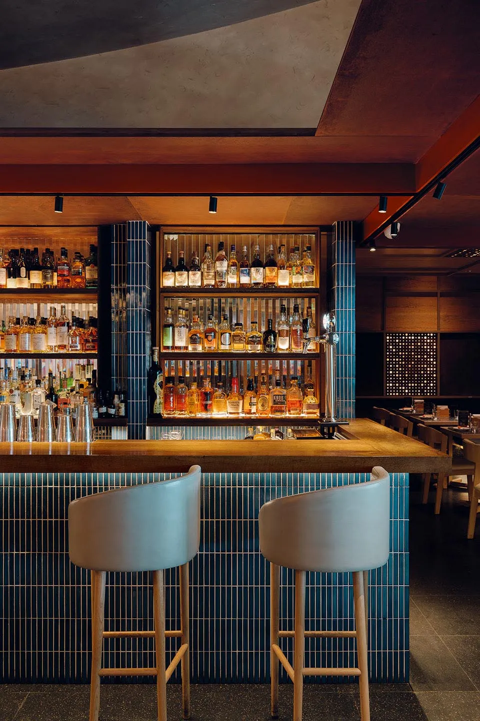 Modern restaurant bar counter featuring blue tiles and a variety of liquor bottles in the background.