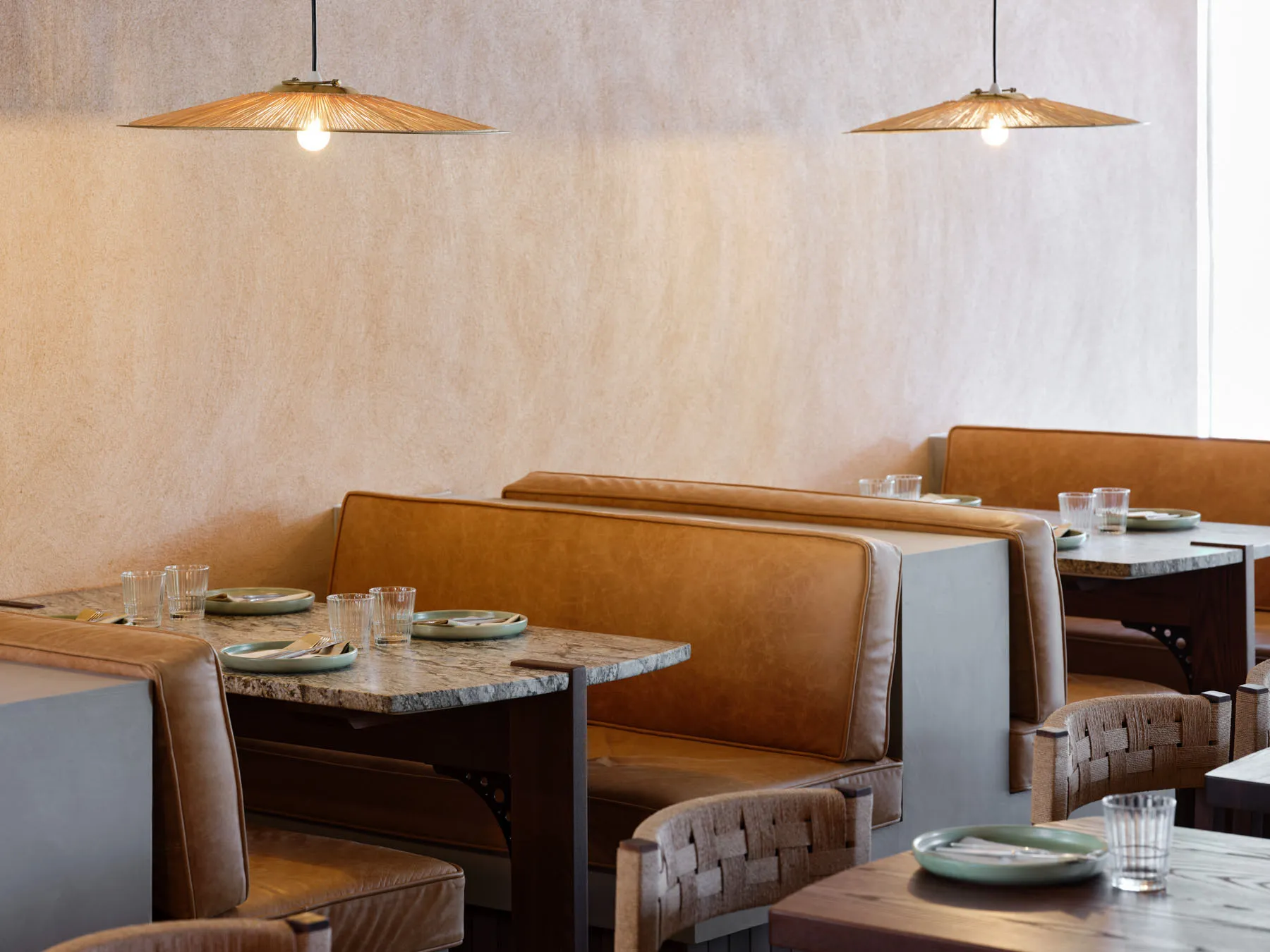 A modern restaurant interior featuring leather seating, wooden tables, and concrete countertops.