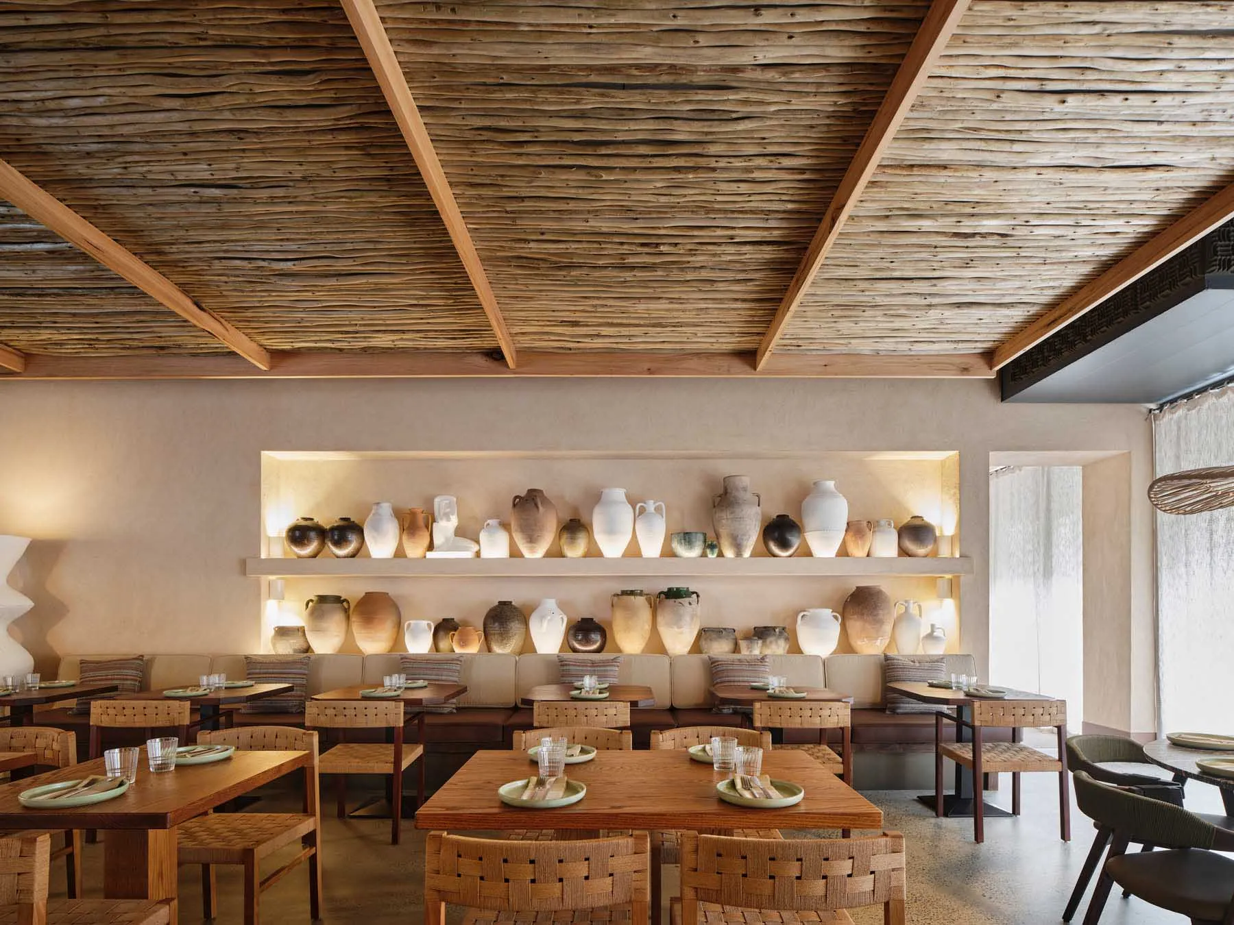 Modern restaurant interior featuring wooden furniture and a wall display of ceramic vases.
