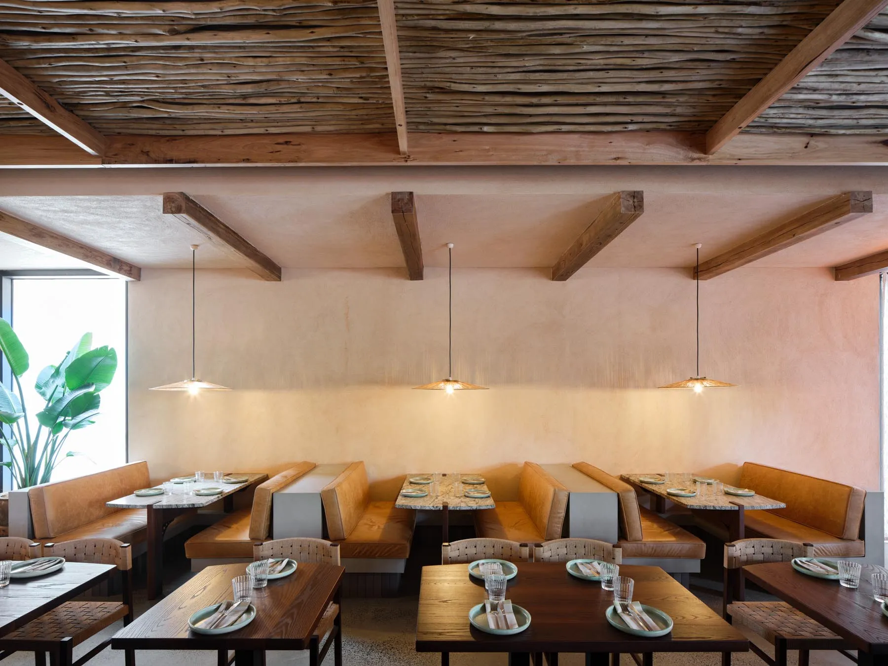 Industrial-style restaurant interior featuring wooden tables, benches, and overhead lighting.